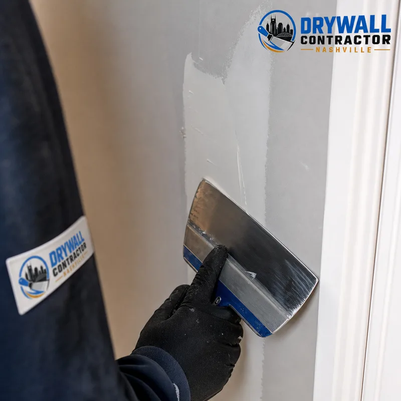 Feathered drywall patch being skim-coated with a wide taping knife near clean trim
