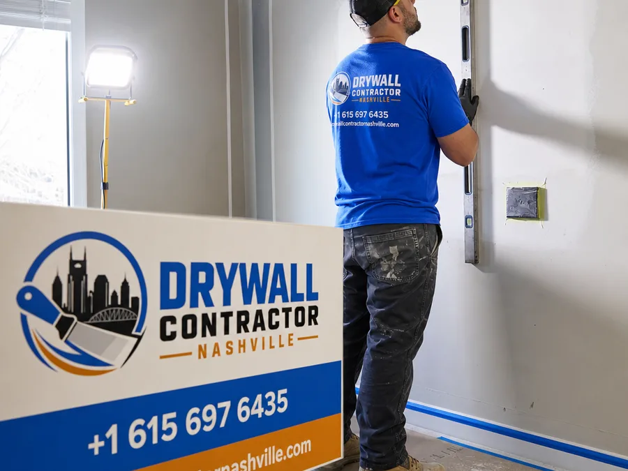 Technician inspecting a protected wall repair area with a straightedge and work light